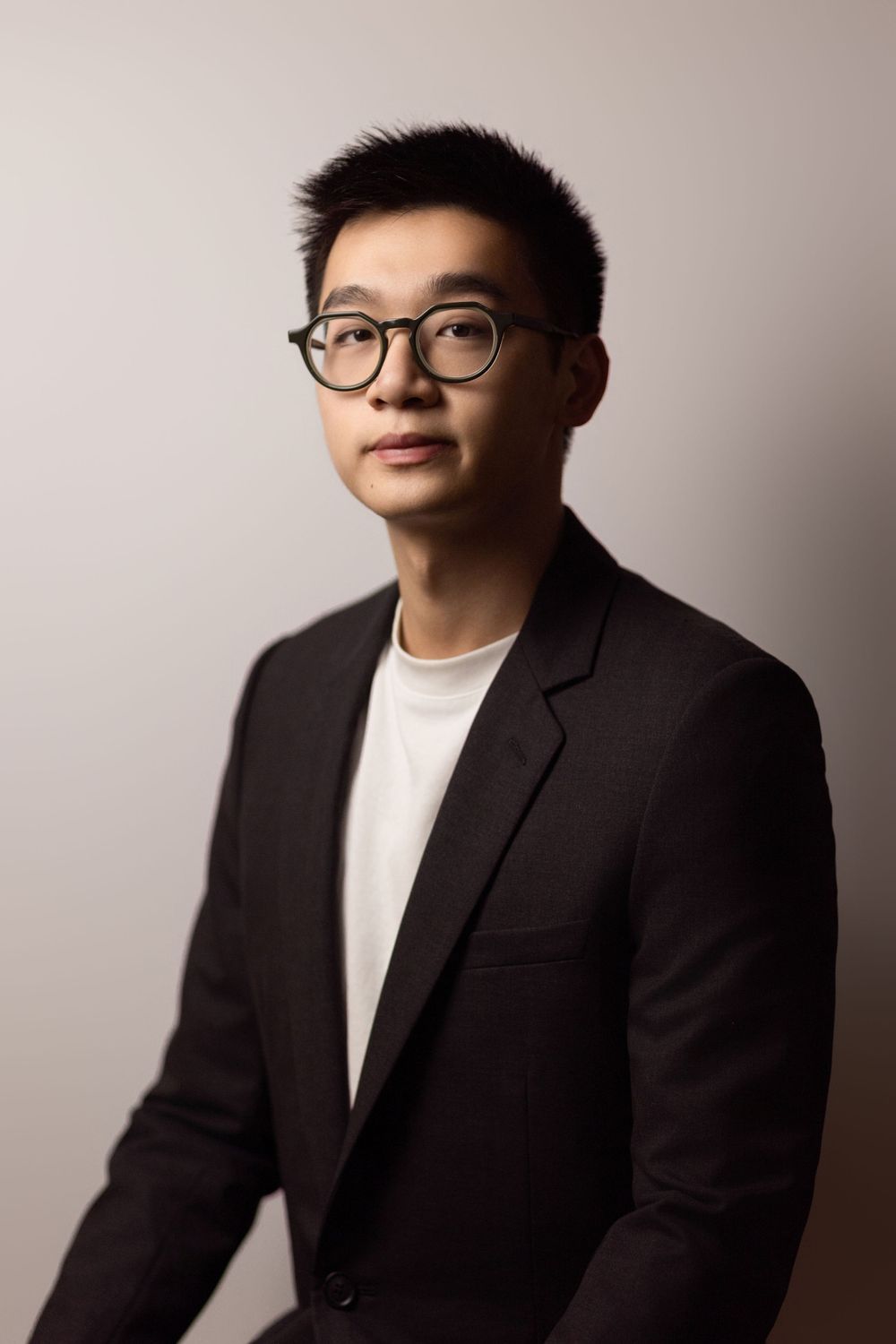 Professional headshot of man in dark blazer and glasses with dramatic side lighting.