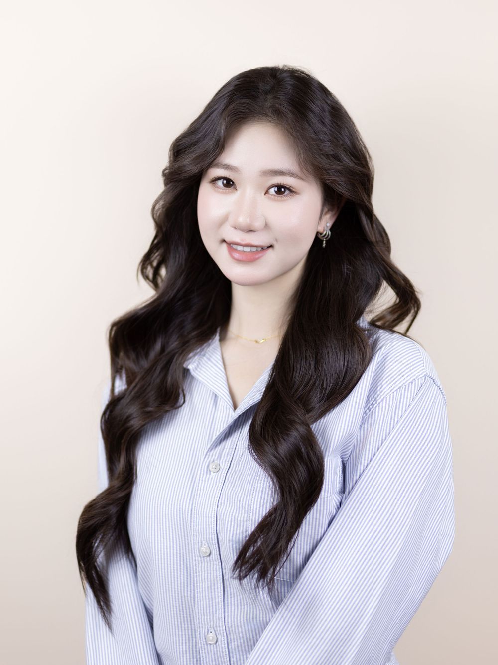 Professional portrait of a smiling woman in a striped button-down shirt with flowing dark wavy hair.