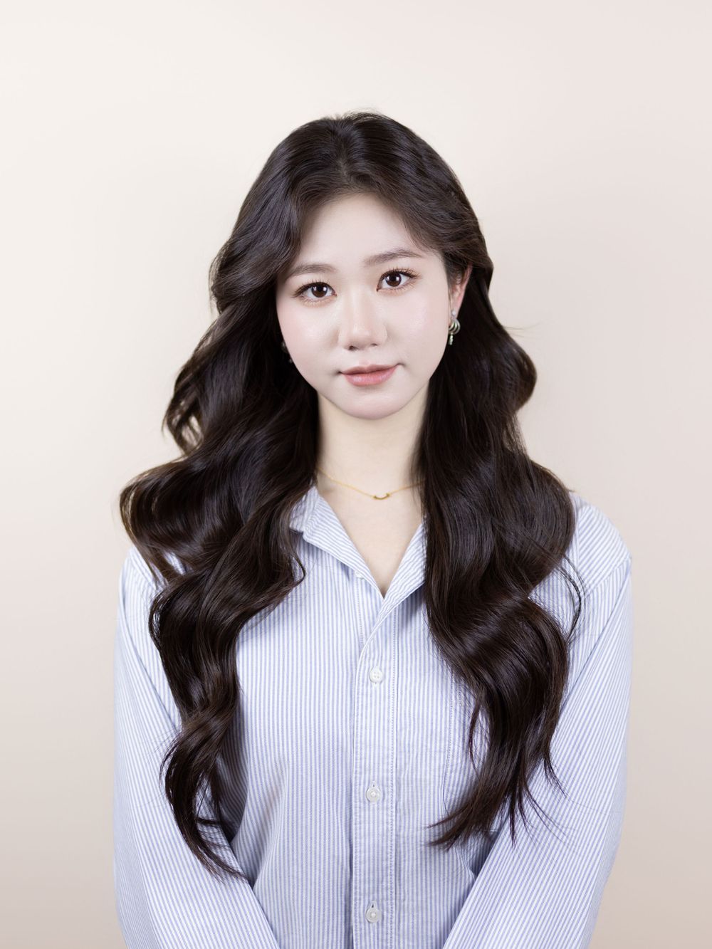 Studio portrait showing long dark wavy hair and business casual attire against light background.