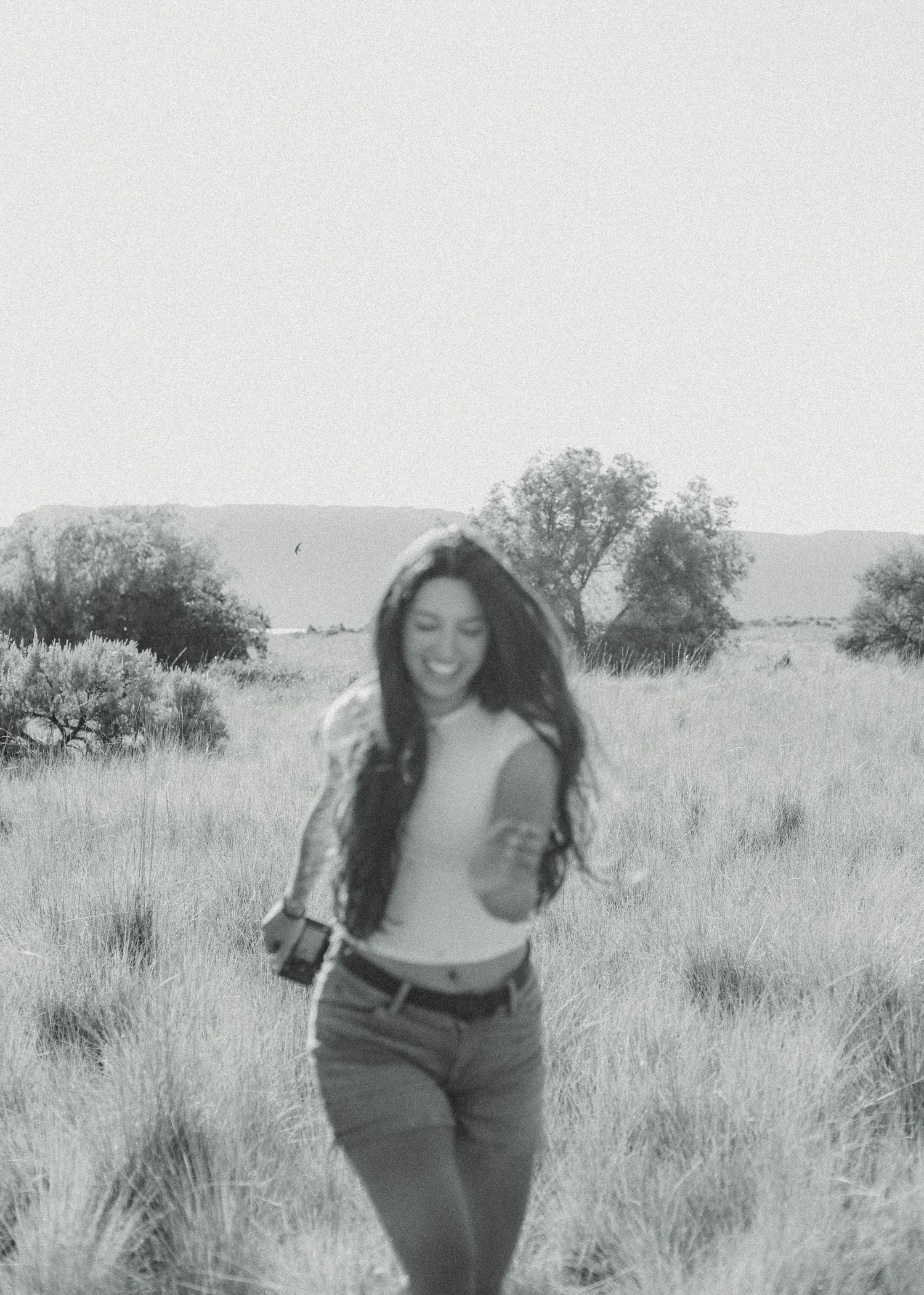A black and white candid photo of someone laughing in a field with long grass.