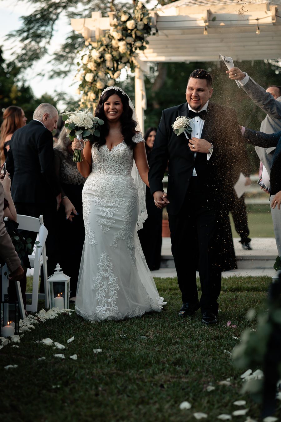 Newlyweds celebrate with joy as guests shower them with confetti under an elegant outdoor wedding pergola.