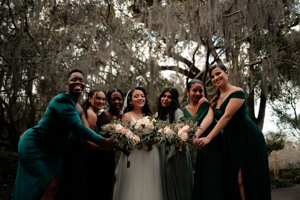 Bride with her bridesmaids, all smiling and holding bouquets in an outdoor setting