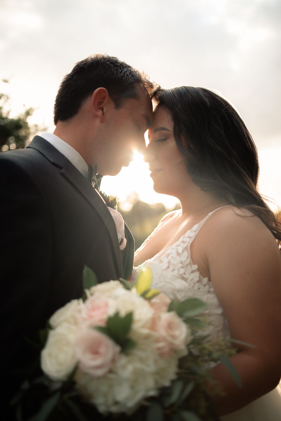 Tender forehead touch between couple during romantic sunset wedding portraits.