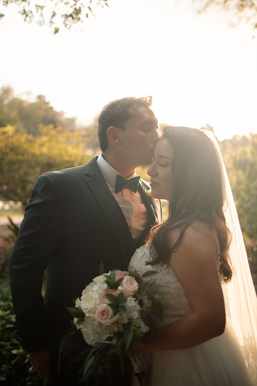Intimate moment between newlyweds captured in golden sunlight with soft pink roses.