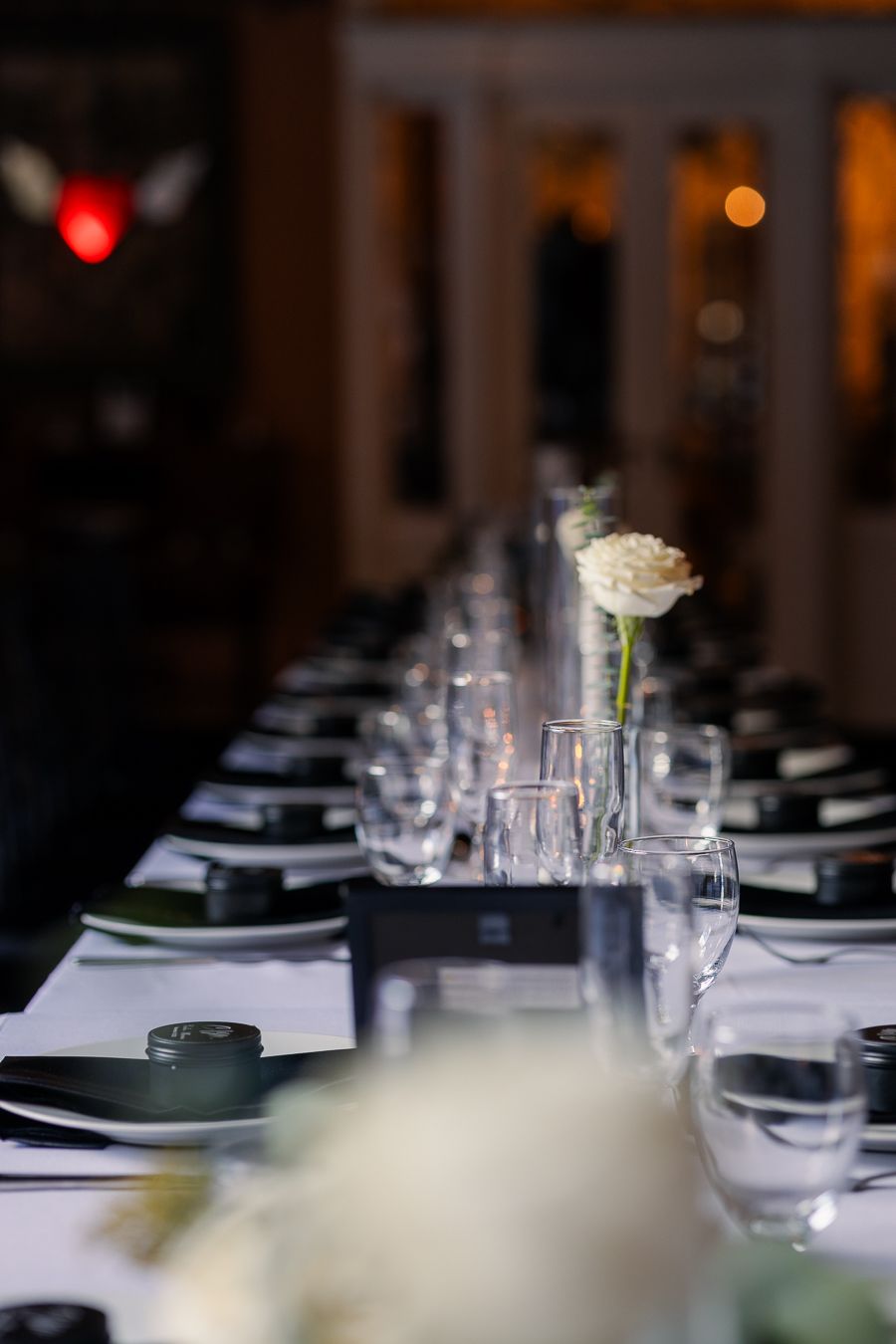 Long wedding reception table with minimalist white flowers, glassware, and elegant black-and-white decor