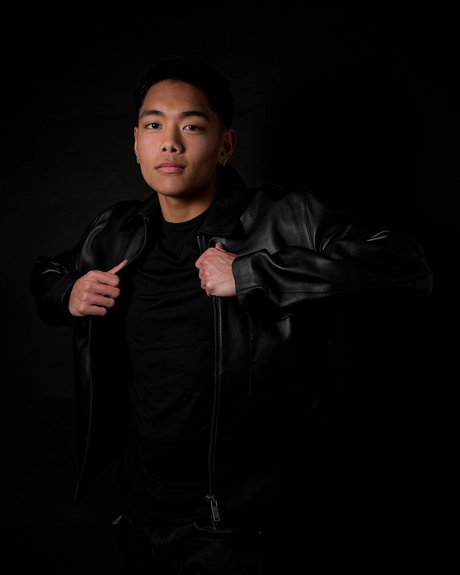Dramatic studio portrait in black leather jacket against dark background.