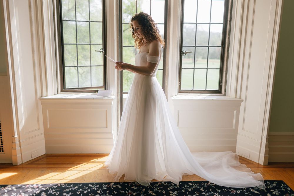 An elegant white wedding gown with a flowing tulle train is illuminated by natural light streaming through tall windows.