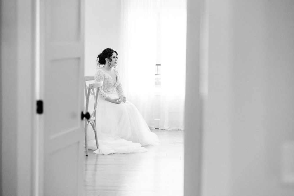 Black and white photo of a bride in a white wedding gown sitting alone in a bright minimalist room.
