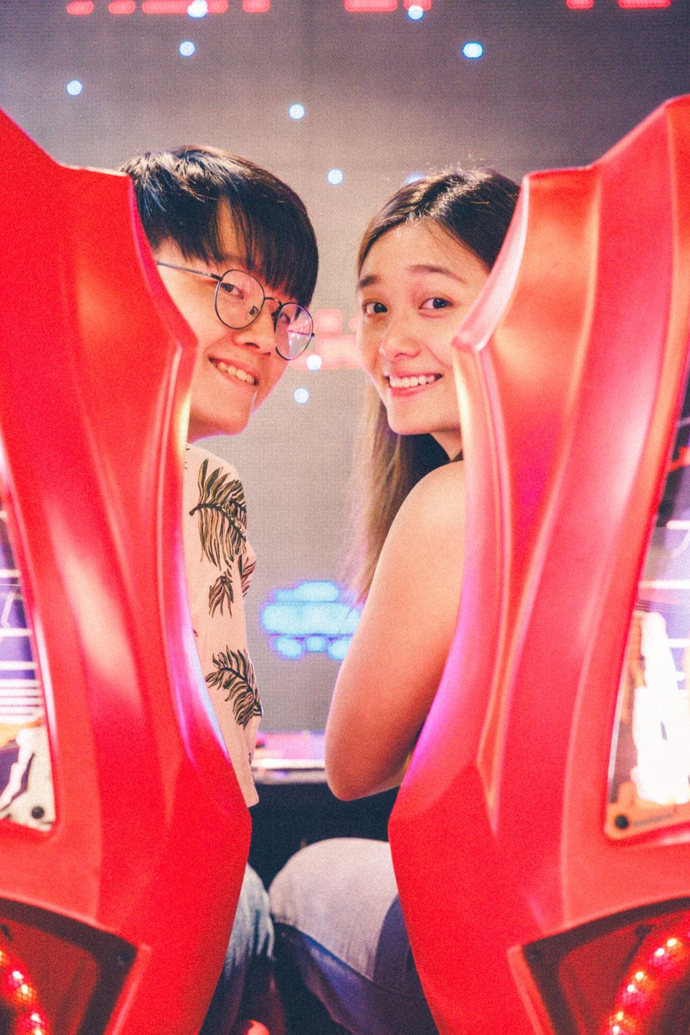 Two people share a fun moment between red arcade machine seats.