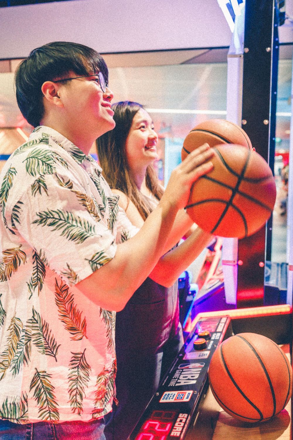 A couple enjoying themselves at an arcade basketball game with neon lights.