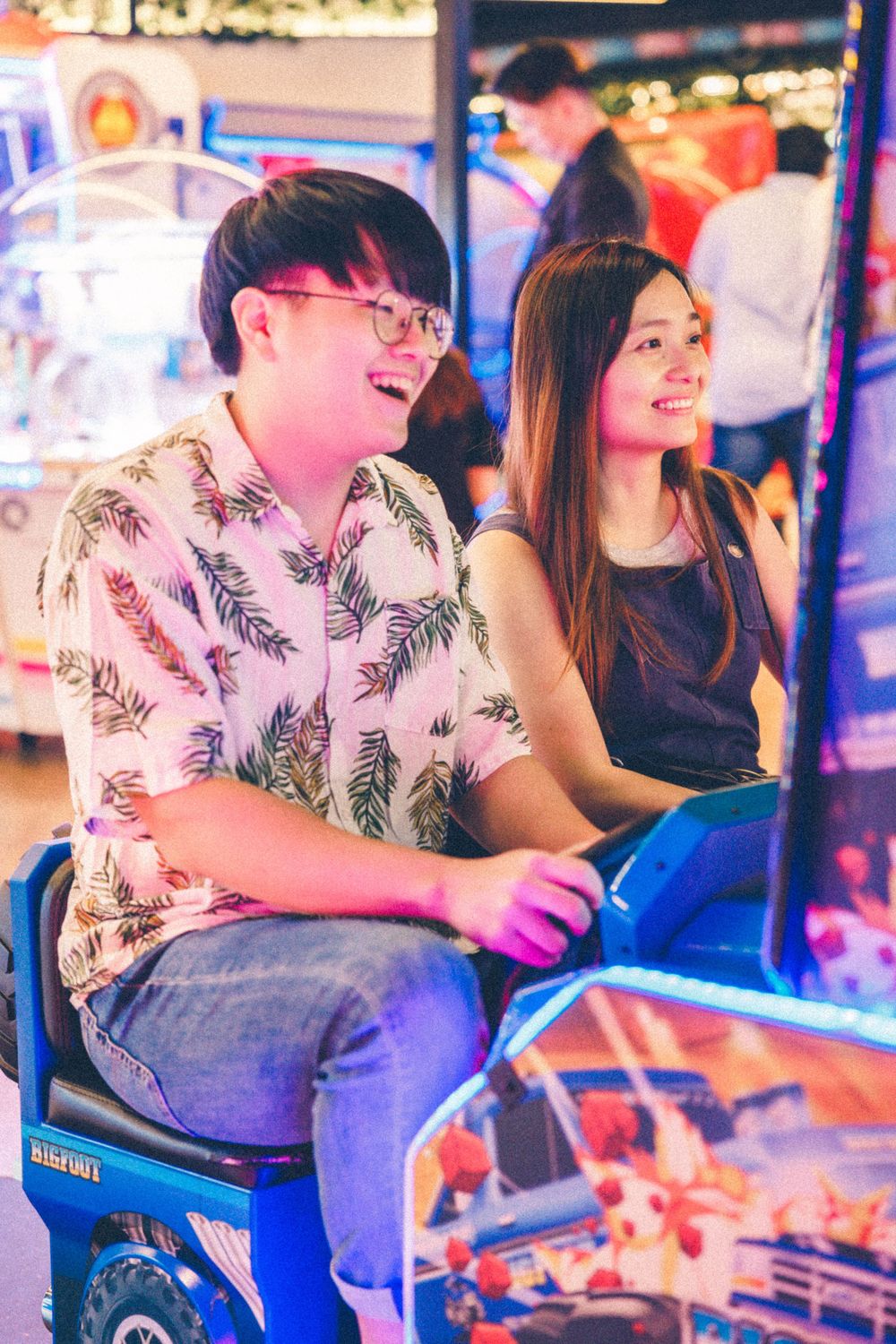 A couple plays arcade games together in a vibrant neon-lit gaming environment.