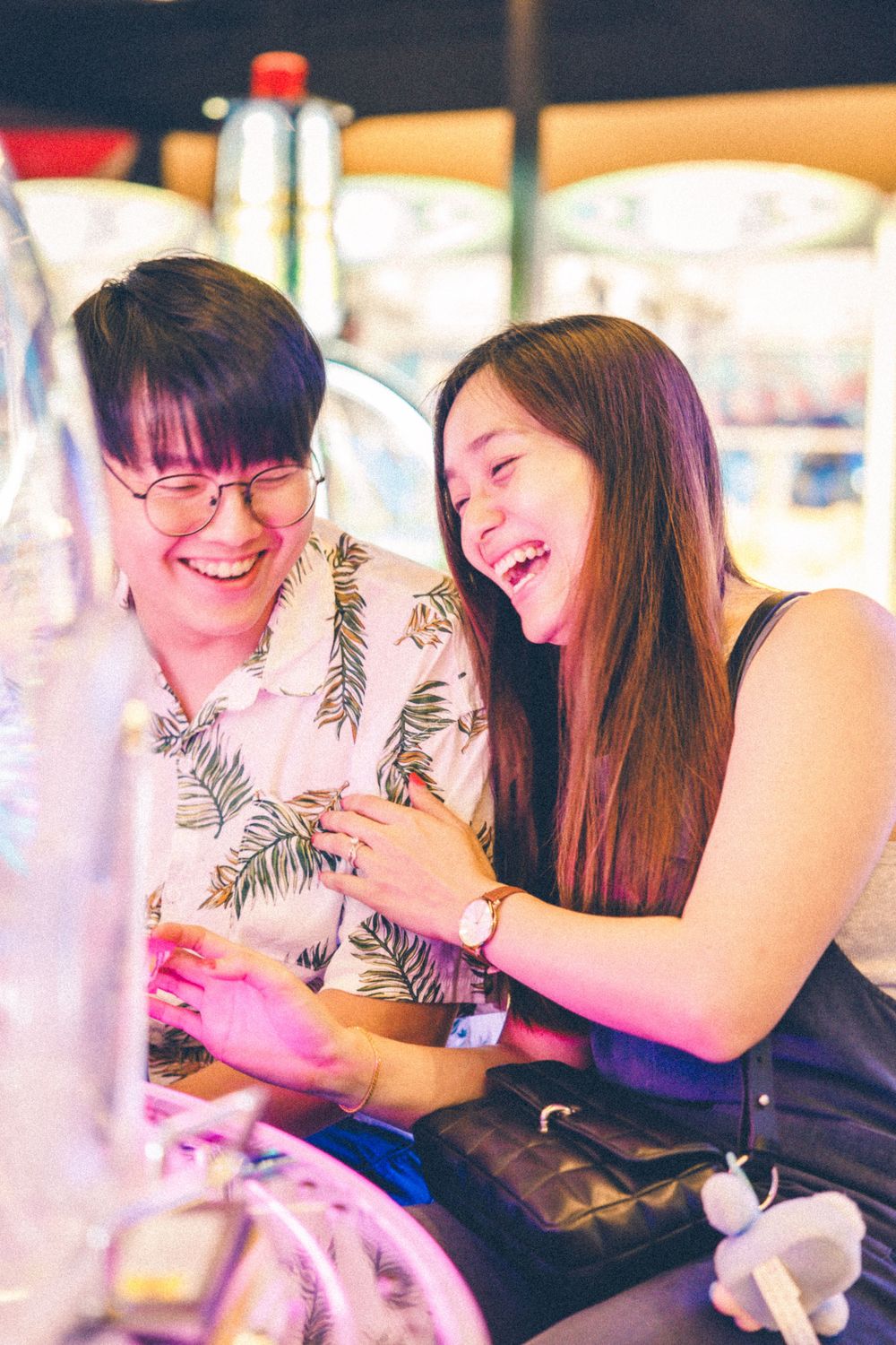 A couple shares a joyful moment together while laughing in a game arcade with neon lights.
