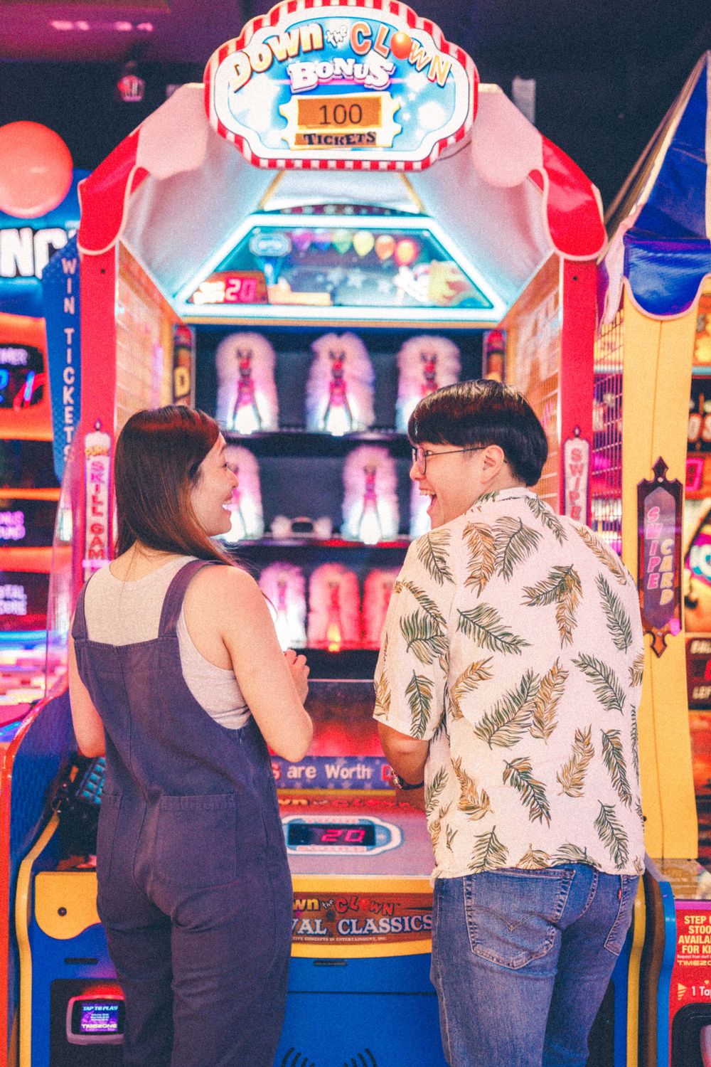 A couple plays arcade games together in a colorful gaming venue with bright signage.