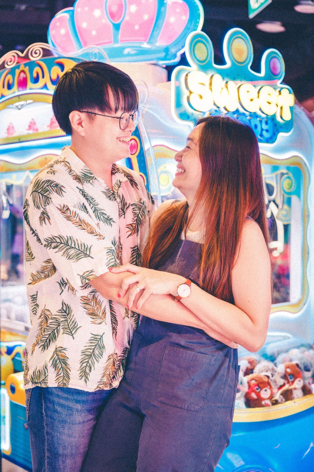 A happy couple embraces in front of colorful arcade games with crown decorations.