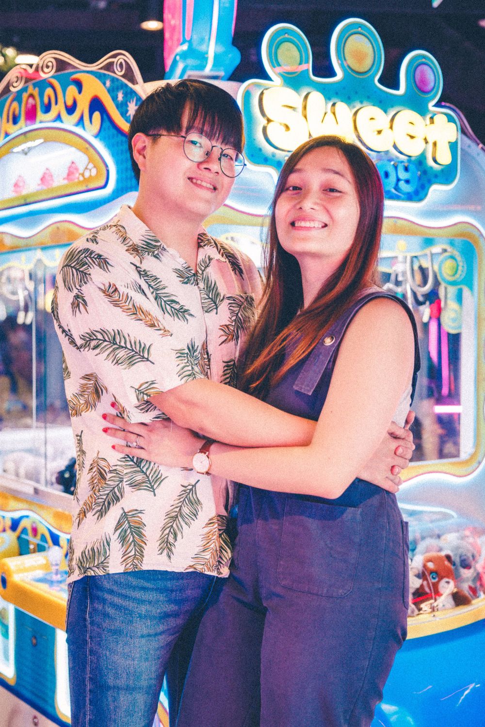 A couple hugs while standing in front of bright arcade games with neon lighting.