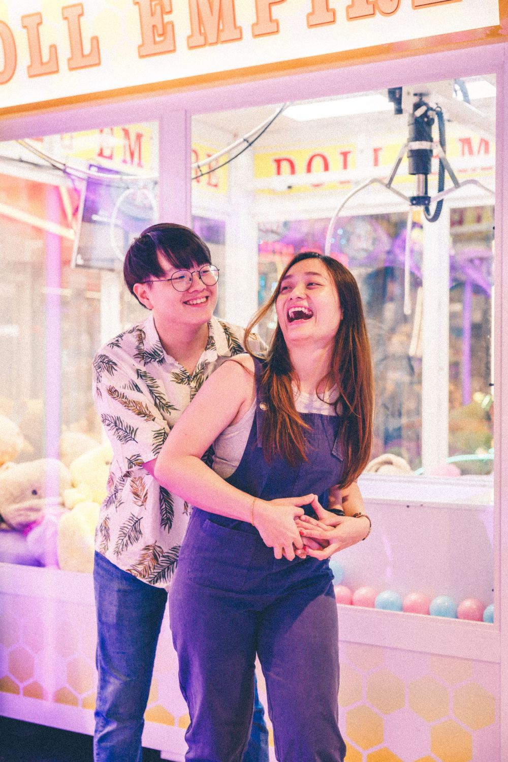 A couple laughs together while playing games at an arcade with pink neon lights.