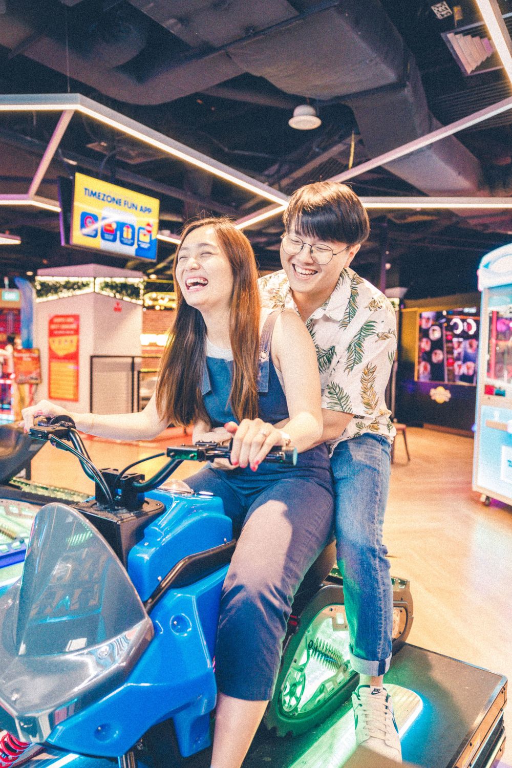 A playful couple enjoys riding a blue arcade motorcycle game together.