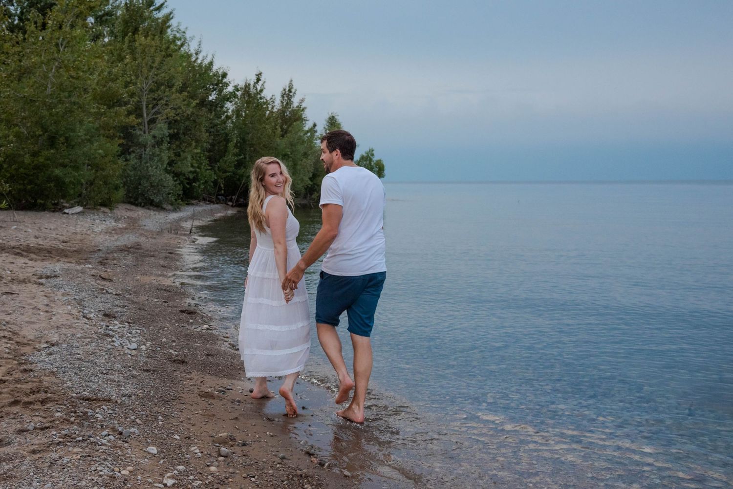 Two people holding hands while walking along a peaceful beach shoreline at dusk.