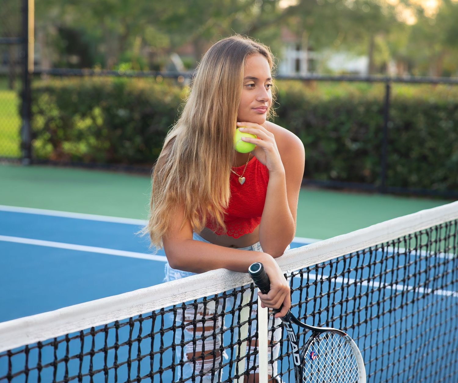 Tennis player with racquet leaning on court net during sunset.