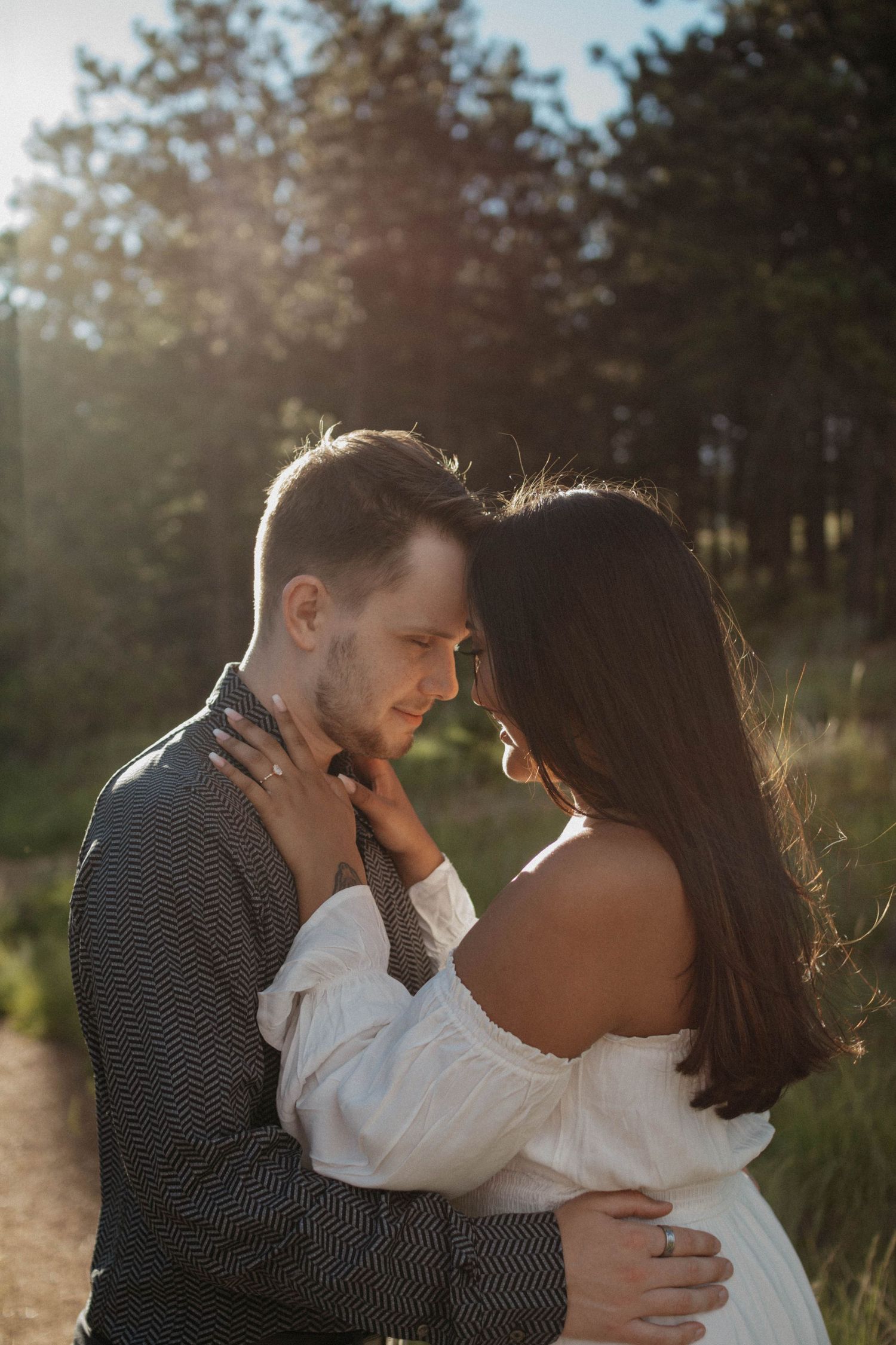 Intimate couple embraces in sunset light with forest backdrop on Colorado mountains. Colorado engagement photoshoot.