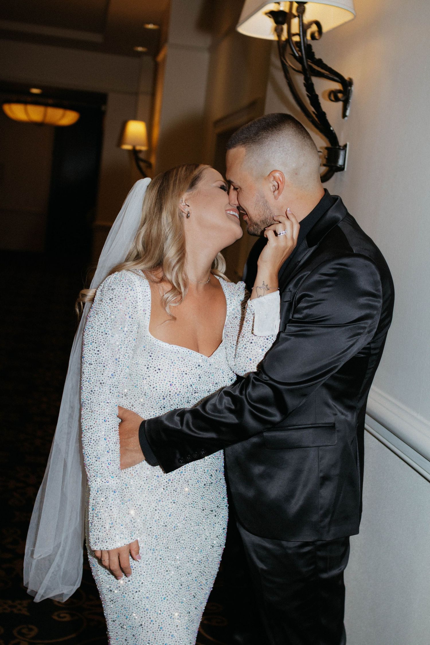 A romantic wedding moment captured in black and white as a couple shares an intimate embrace in a dimly lit hallway.