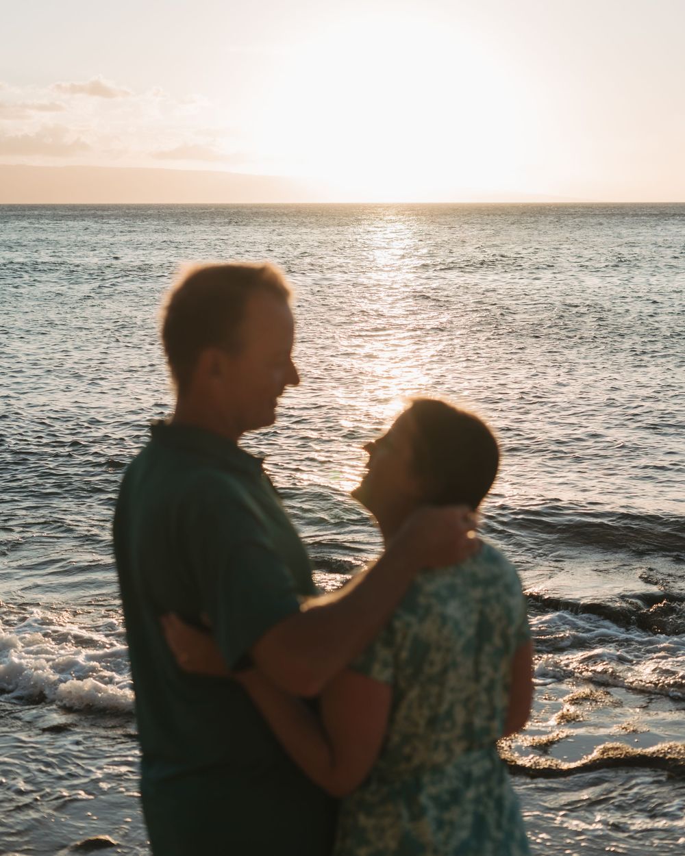 Two silhouettes dance together against a sunset ocean backdrop creating a romantic seaside moment.