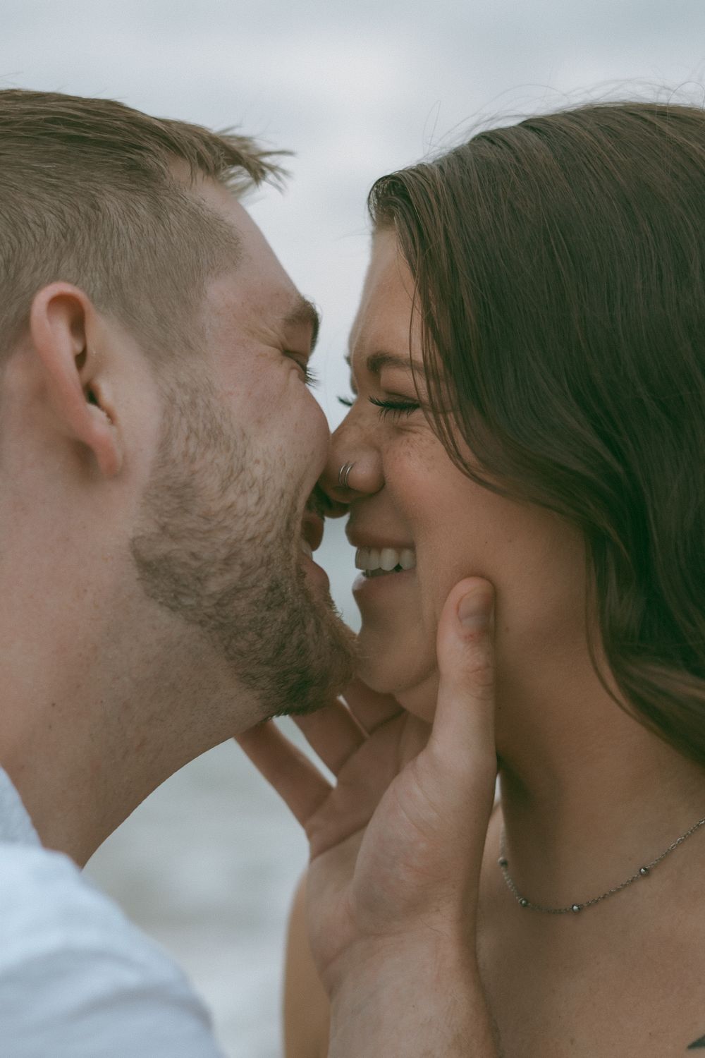 Smiling couple almost kissing closely on the beach, man gently holding woman's face.