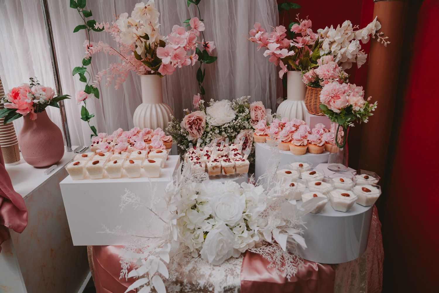 An elegant dessert table decorated with pink flowers, white vases, and delicate pastries.