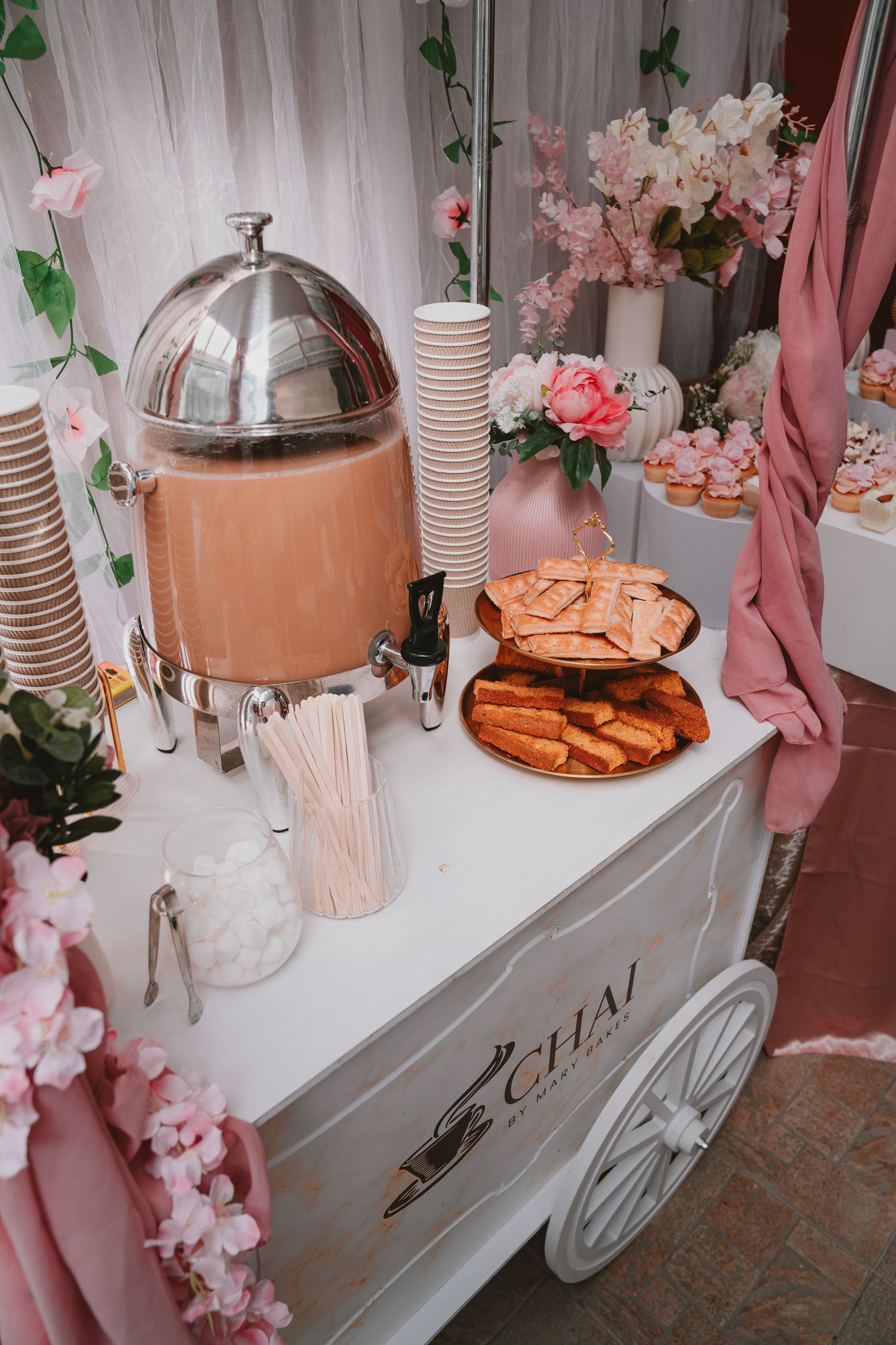 A vintage-style beverage cart with pink decorations and refreshments at a wedding reception.