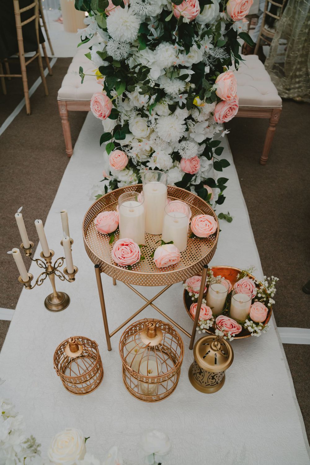Elegant wedding decor featuring white candles and pink roses on a gold accent table with vintage style elements.