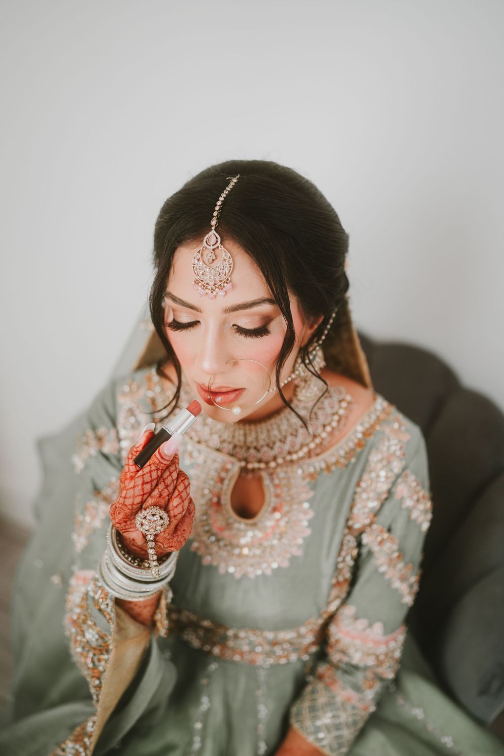 Close-up of intricate bridal jewelry and traditional South Asian wedding attire in sage green.