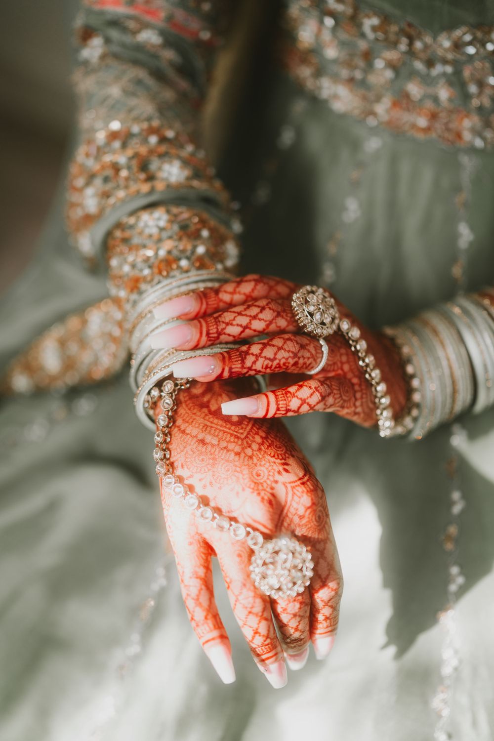 Close-up of henna-adorned hands with diamond bangles and traditional bridal jewelry.