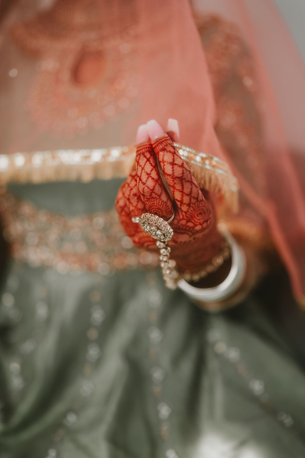 Close-up of henna-decorated hands holding jewelry through a sheer red veil.