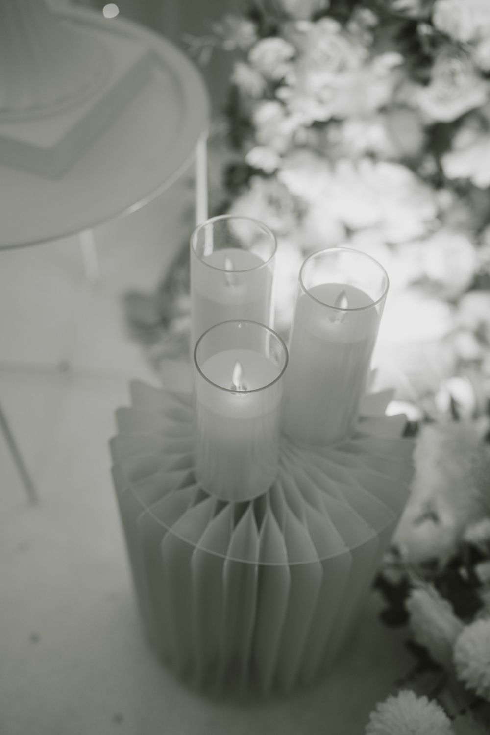 White pillar candles arranged on a pleated base with soft floral decorations in black and white.