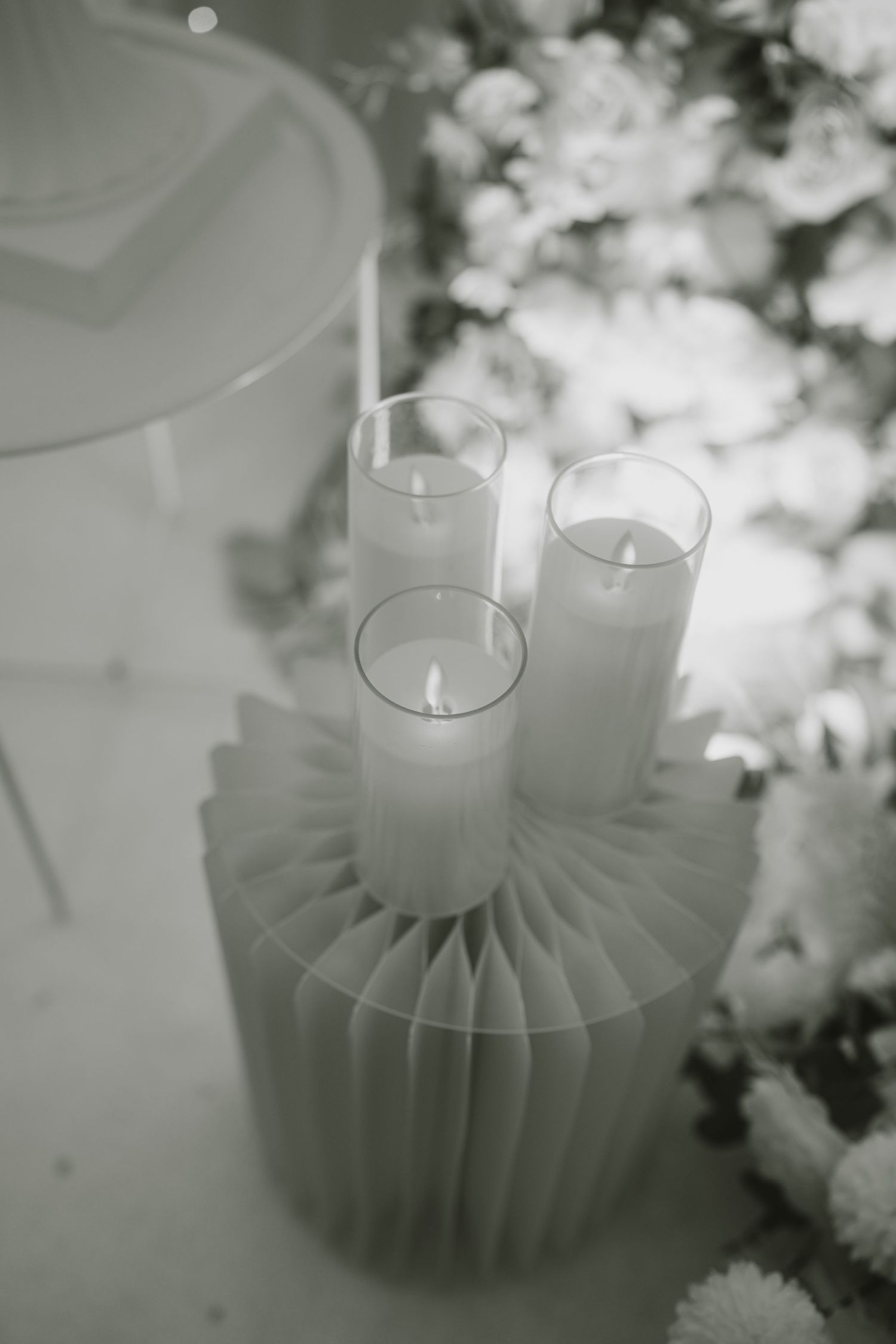 White pillar candles arranged on a pleated base with soft floral decorations in black and white.
