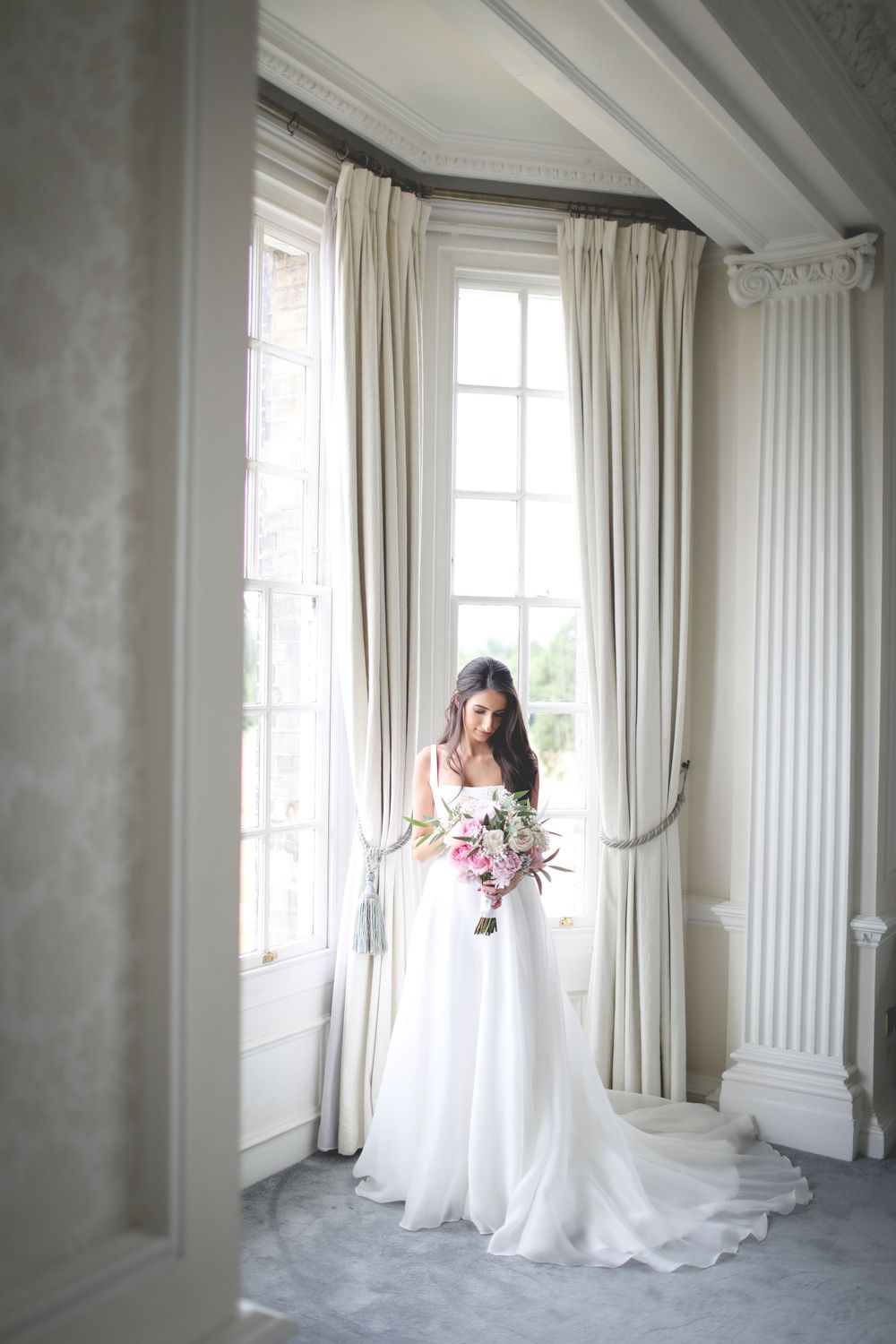 Elegant bridal portrait in a sunlit room with floor-length white curtains and classic architectural details. Hindu Wedding Photography