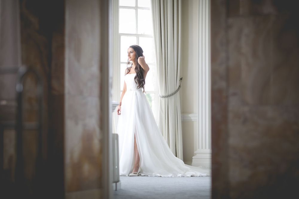 Artistic side view of a wedding dress through doorway in bright natural light. Hedsor House Wedding Asian Wedding Photography