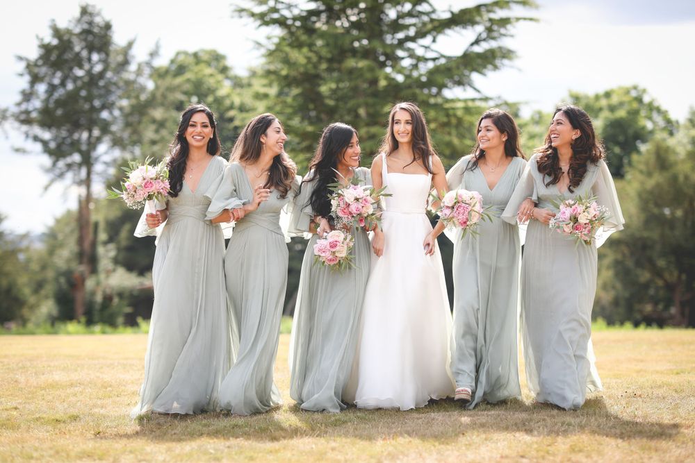Bridesmaids in flowing gray dresses pose with bride outdoors in natural setting. Hedsor House Wedding