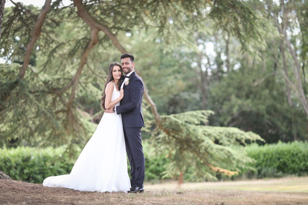 A romantic wedding couple poses under evergreen trees in an outdoor garden setting. Hedsor House Wedding, Indian Wedding Photography