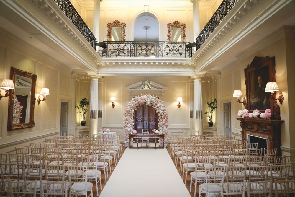Luxurious wedding ceremony setup with white aisle runner and gold chairs in grand ballroom. Hindu Wedding Photography