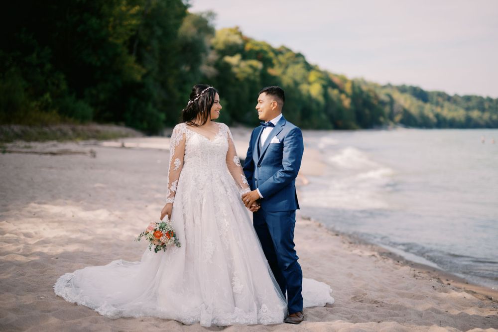 A romantic beach wedding portrait features a couple holding hands while standing along the water's edge.