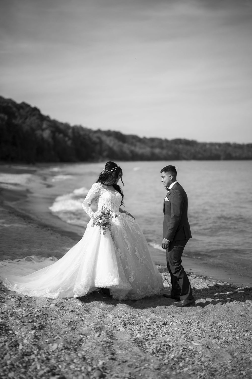 A black and white wedding photo of a couple on a scenic beach with rolling waves and cliffs in the background.