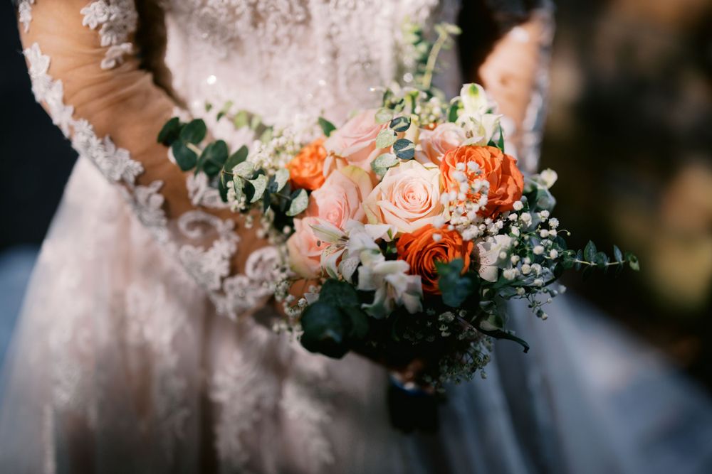 A delicate bridal bouquet features peach roses, white baby's breath, and eucalyptus leaves against a white wedding dress.