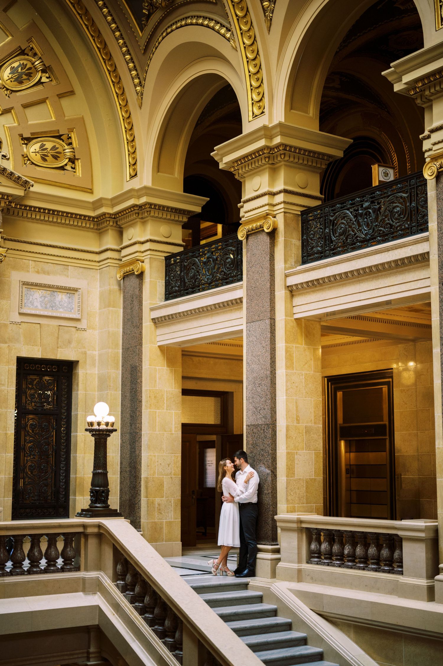 Elegant architectural interior of historic building with grand staircase, ornate columns and arched ceilings in cream and gold tones.