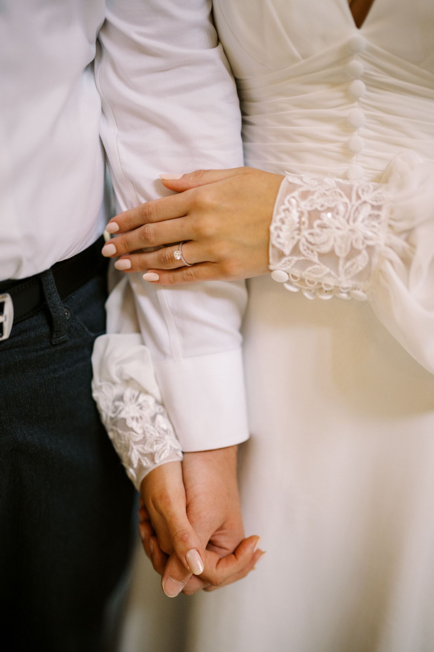 A close-up of hands with an engagement ring showing lace sleeve details of a wedding dress.