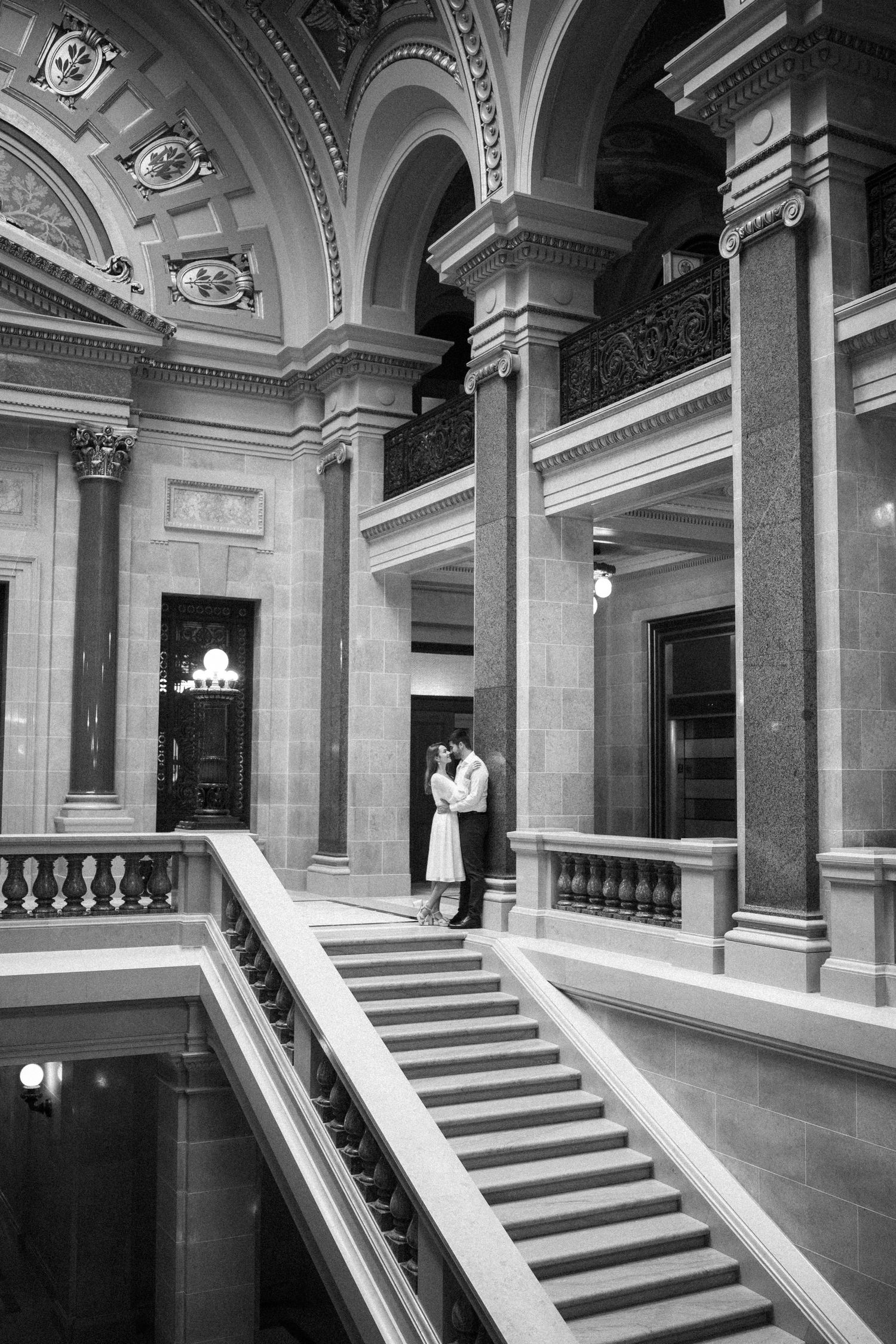 Black and white photo of a couple standing on ornate marble stairs in a historic building.