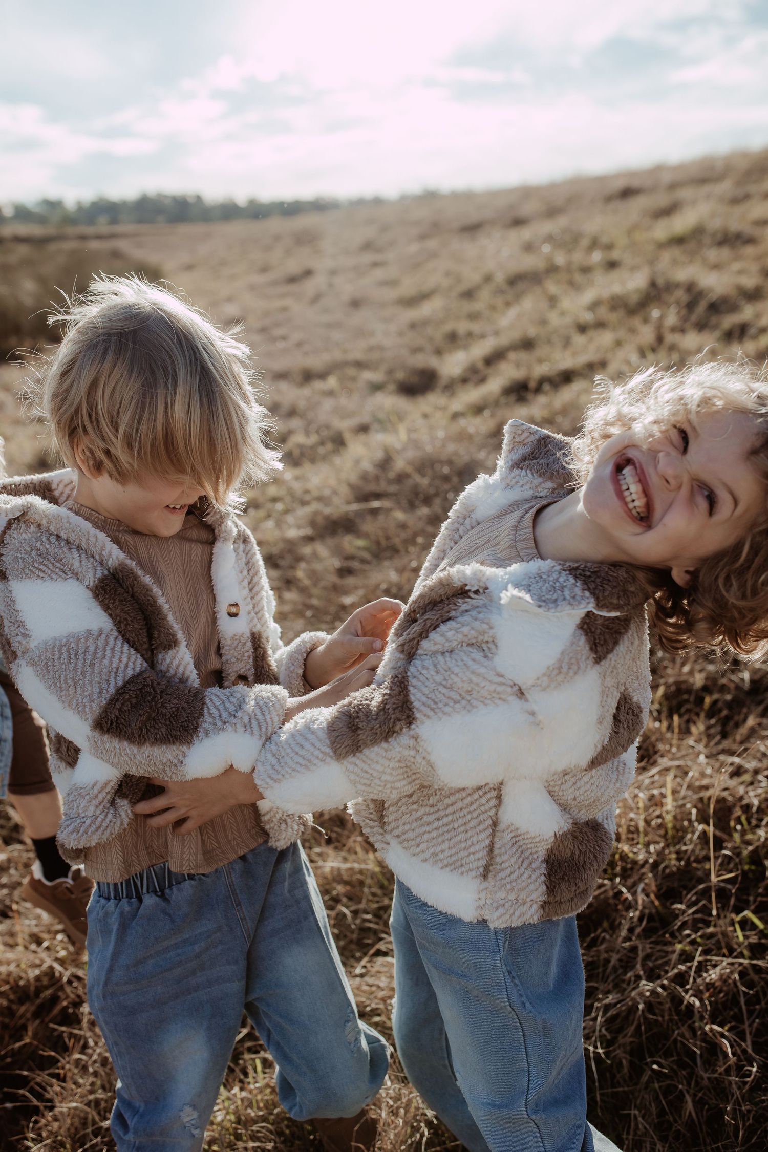 Two children in matching checkered sweaters laugh together in a field.