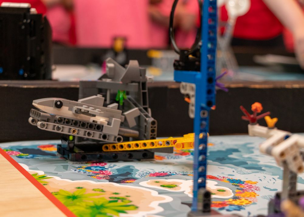 Close up of LEGO robotics pieces and technical components on a colorful play surface with blue support beams.