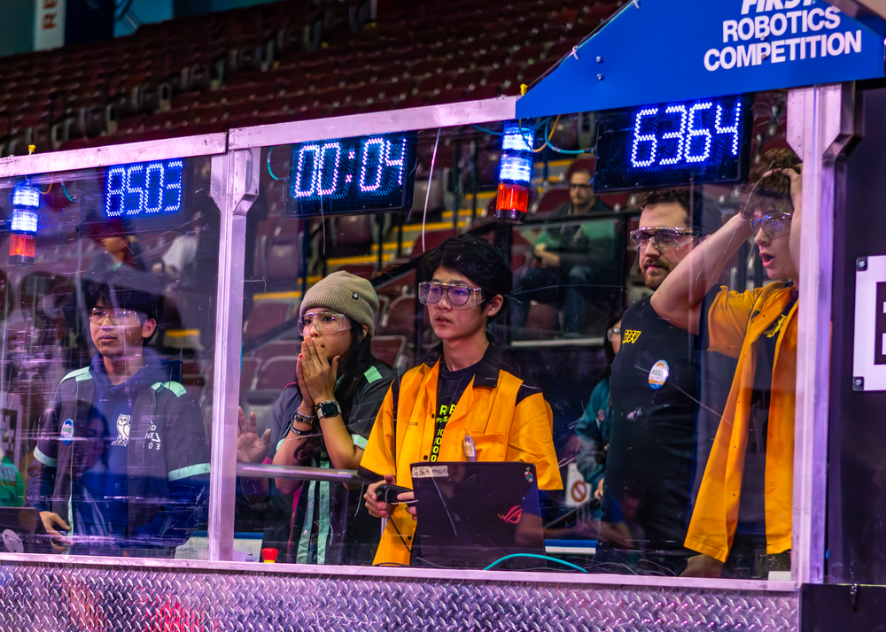 Students control their robot during a FIRST Robotics Competition match with scoreboard displaying time.