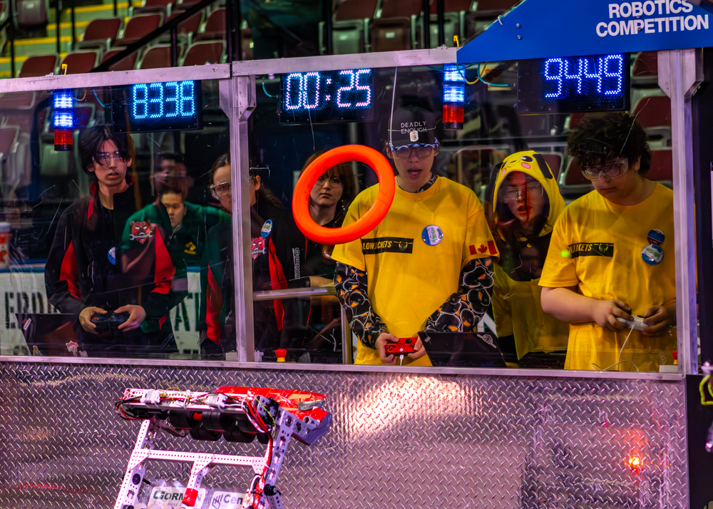 Robotics competition participants monitor digital displays and equipment at a competitive event.